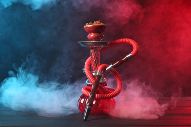 Photo of Hookah on wooden table with smoke in color lights against black background