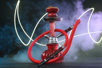 Photo of Hookah on wooden table with smoke in color lights against black background