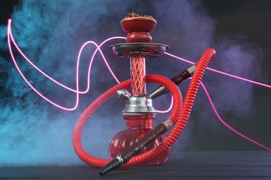Photo of Hookah on wooden table with smoke in color lights against black background