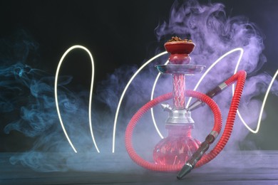 Photo of Hookah on wooden table with smoke in color lights against black background