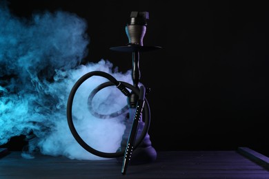 Photo of Hookah on wooden table with smoke in color lights against black background