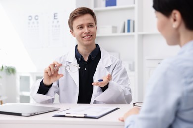 Photo of Ophthalmologist consulting woman at white table in clinic