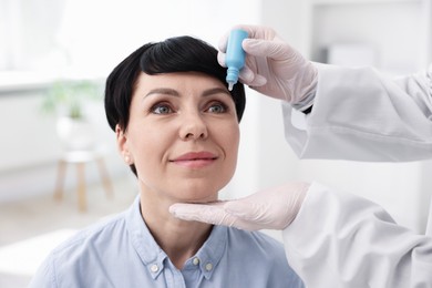 Photo of Ophthalmologist applying medical drops onto patient's eye in clinic, closeup