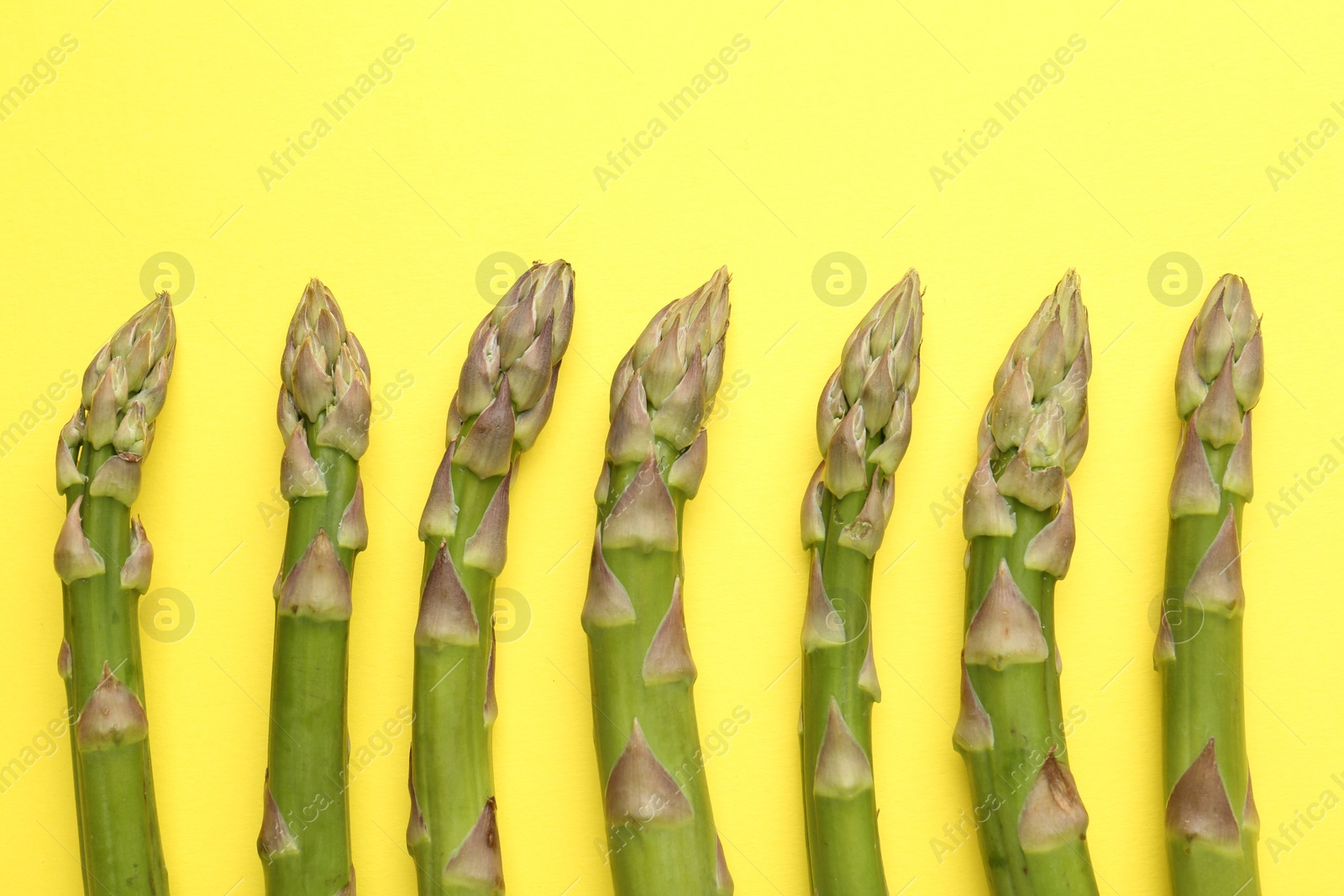 Fresh ripe raw asparagus on yellow background, flat lay Photo of Fresh ripe raw asparagus on yellow background, flat lay