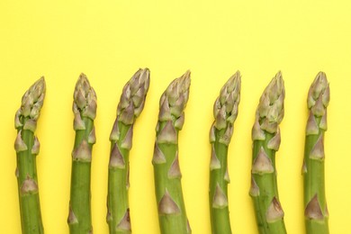 Photo of Fresh ripe raw asparagus on yellow background, flat lay