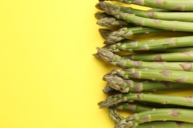 Photo of Fresh ripe raw asparagus on yellow background, flat lay. Space for text
