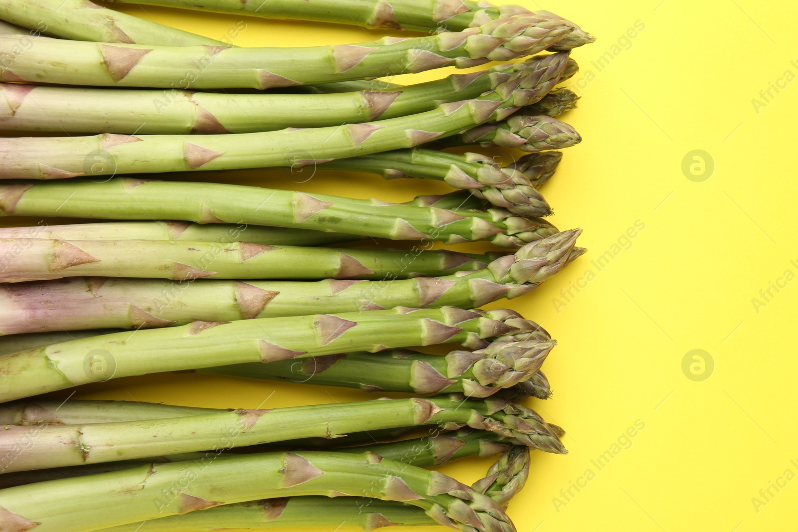 Fresh ripe raw asparagus on yellow background, flat lay Photo of Fresh ripe raw asparagus on yellow background, flat lay