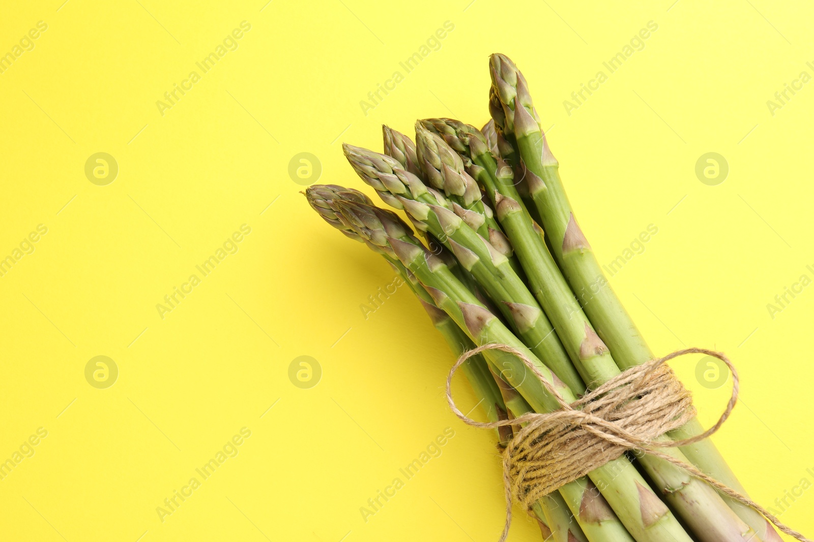 Tied raw asparagus on yellow background, top view. Space for text Photo of Tied raw asparagus on yellow background, top view. Space for text