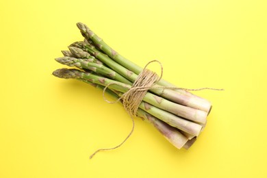 Photo of Tied raw asparagus on yellow background, top view