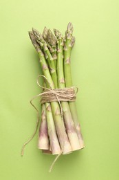 Photo of Tied raw asparagus on green background, top view