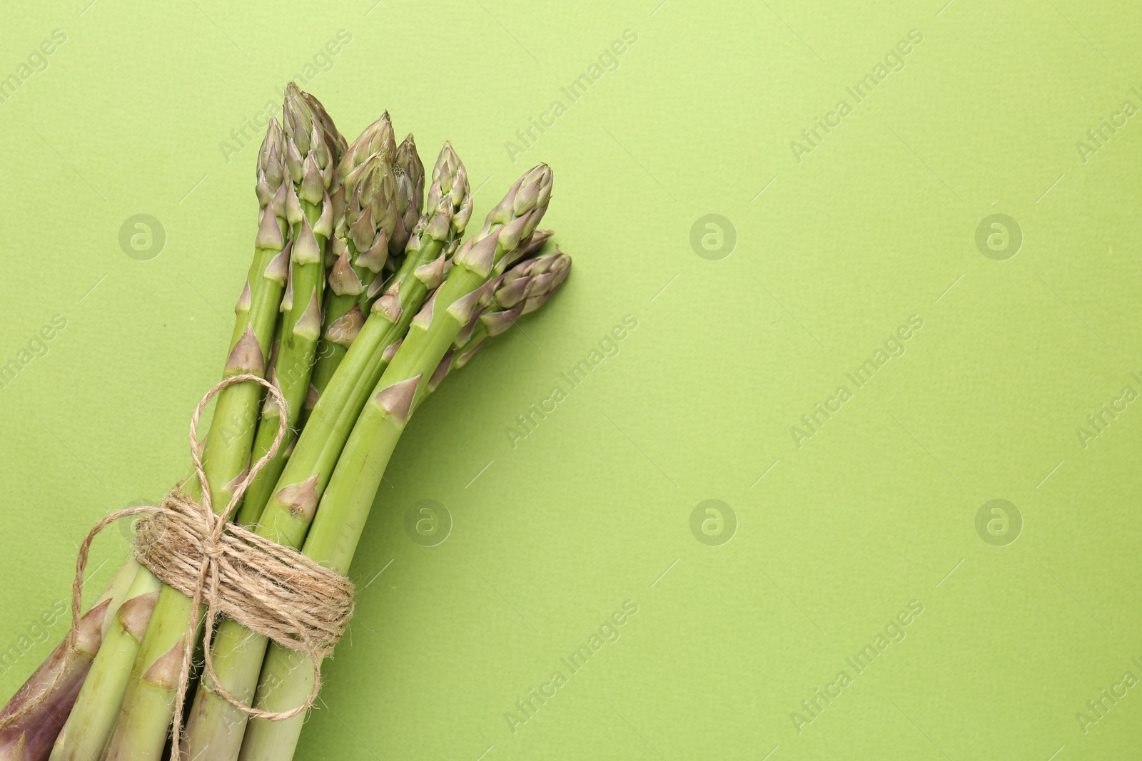 Tied raw asparagus on green background, top view. Space for text Photo of Tied raw asparagus on green background, top view. Space for text