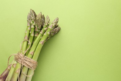 Photo of Tied raw asparagus on green background, top view. Space for text