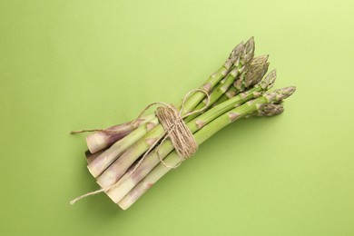 Photo of Tied raw asparagus on green background, top view