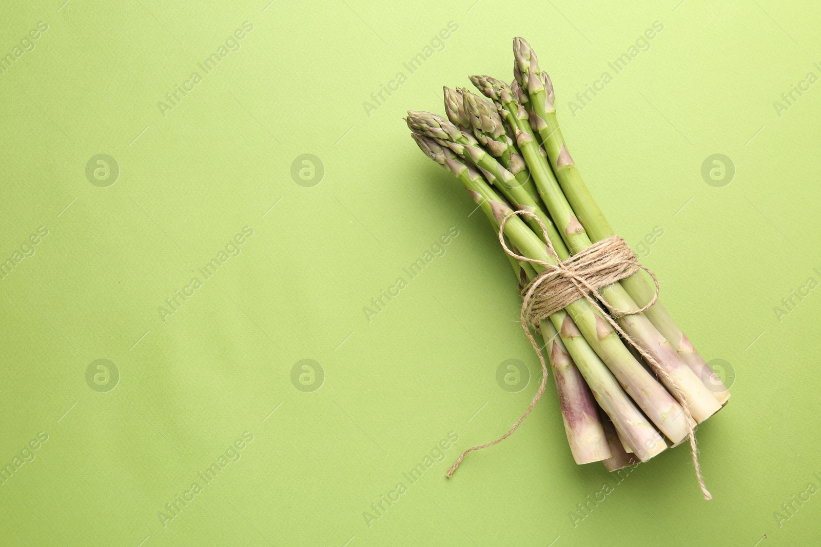 Tied raw asparagus on green background, top view. Space for text Photo of Tied raw asparagus on green background, top view. Space for text