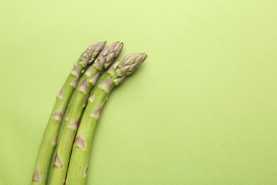 Photo of Fresh ripe raw asparagus on green background, top view. Space for text