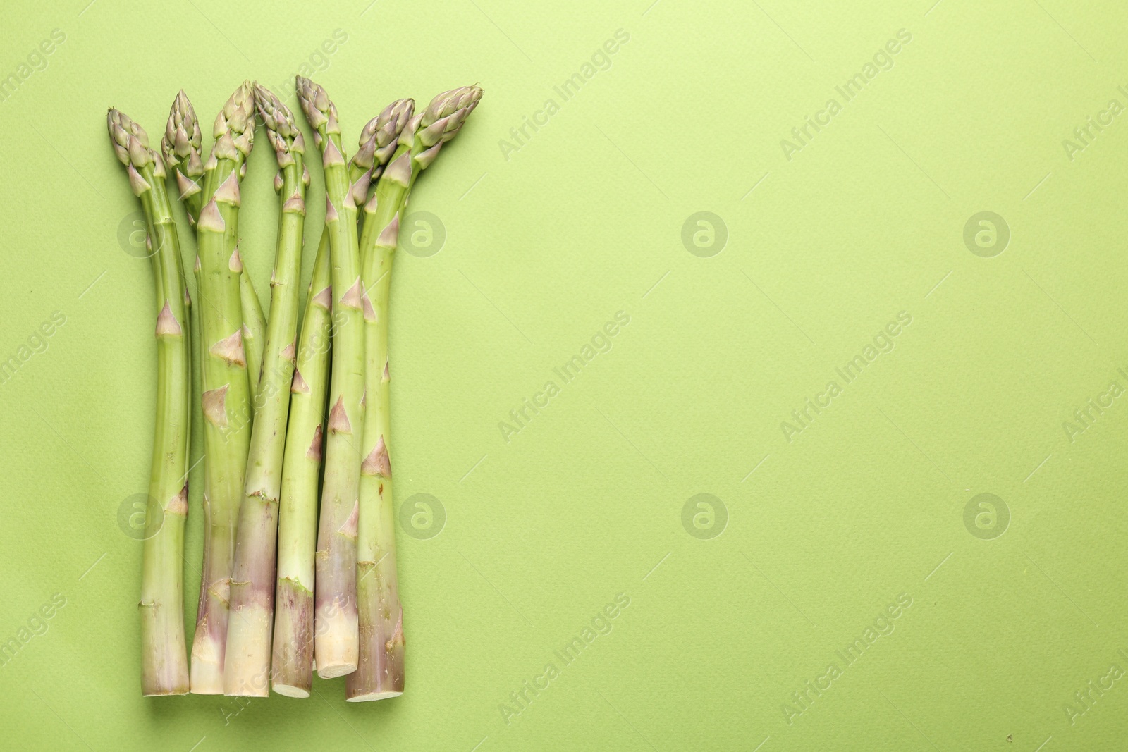 Fresh ripe raw asparagus on green background, top view. Space for text Photo of Fresh ripe raw asparagus on green background, top view. Space for text