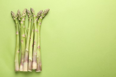 Photo of Fresh ripe raw asparagus on green background, top view. Space for text