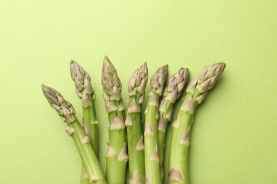 Photo of Fresh ripe raw asparagus on green background, top view