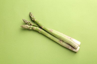 Photo of Fresh ripe raw asparagus on green background, top view