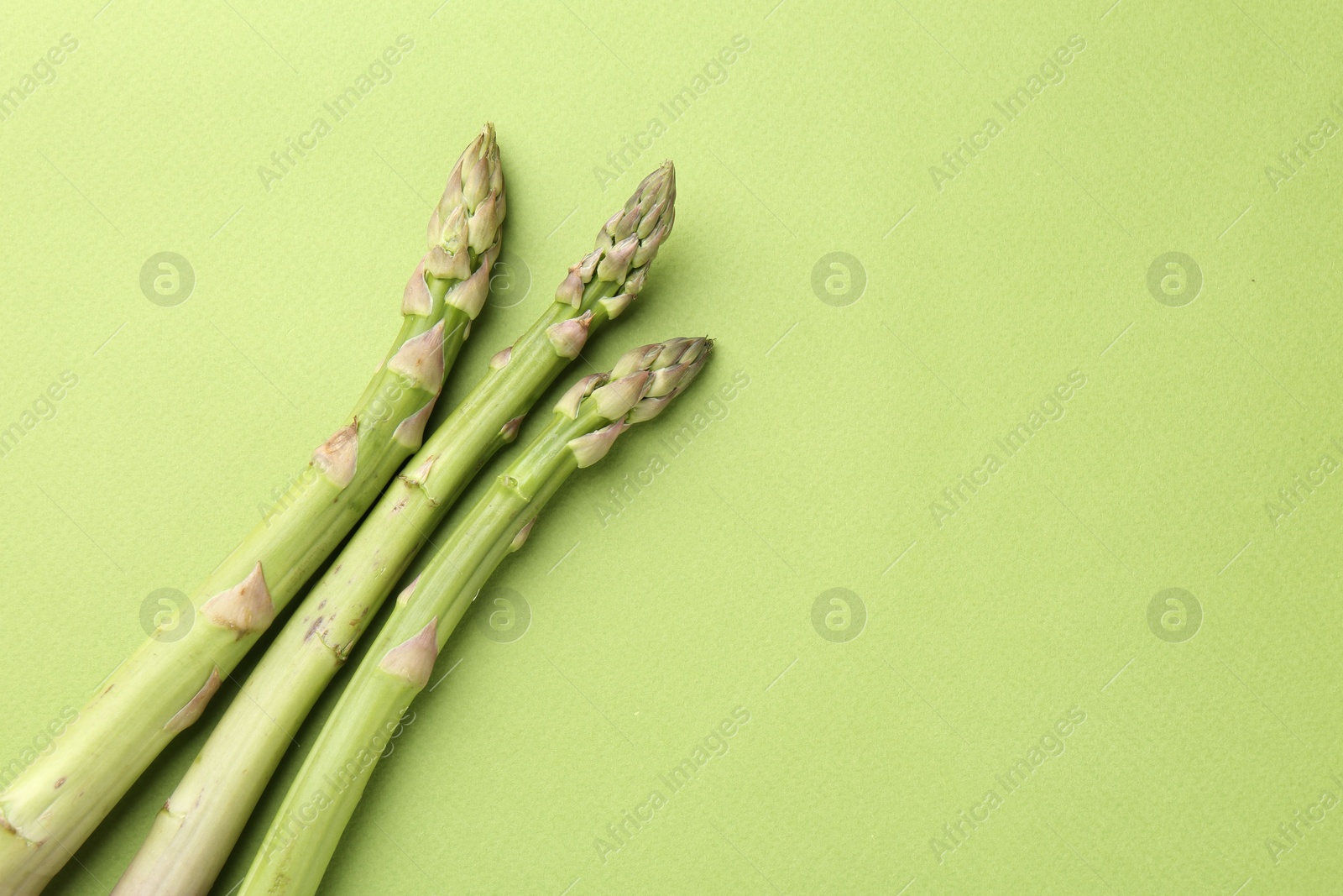 Fresh ripe raw asparagus on green background, top view. Space for text Photo of Fresh ripe raw asparagus on green background, top view. Space for text