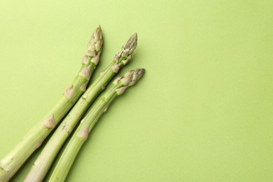 Photo of Fresh ripe raw asparagus on green background, top view. Space for text