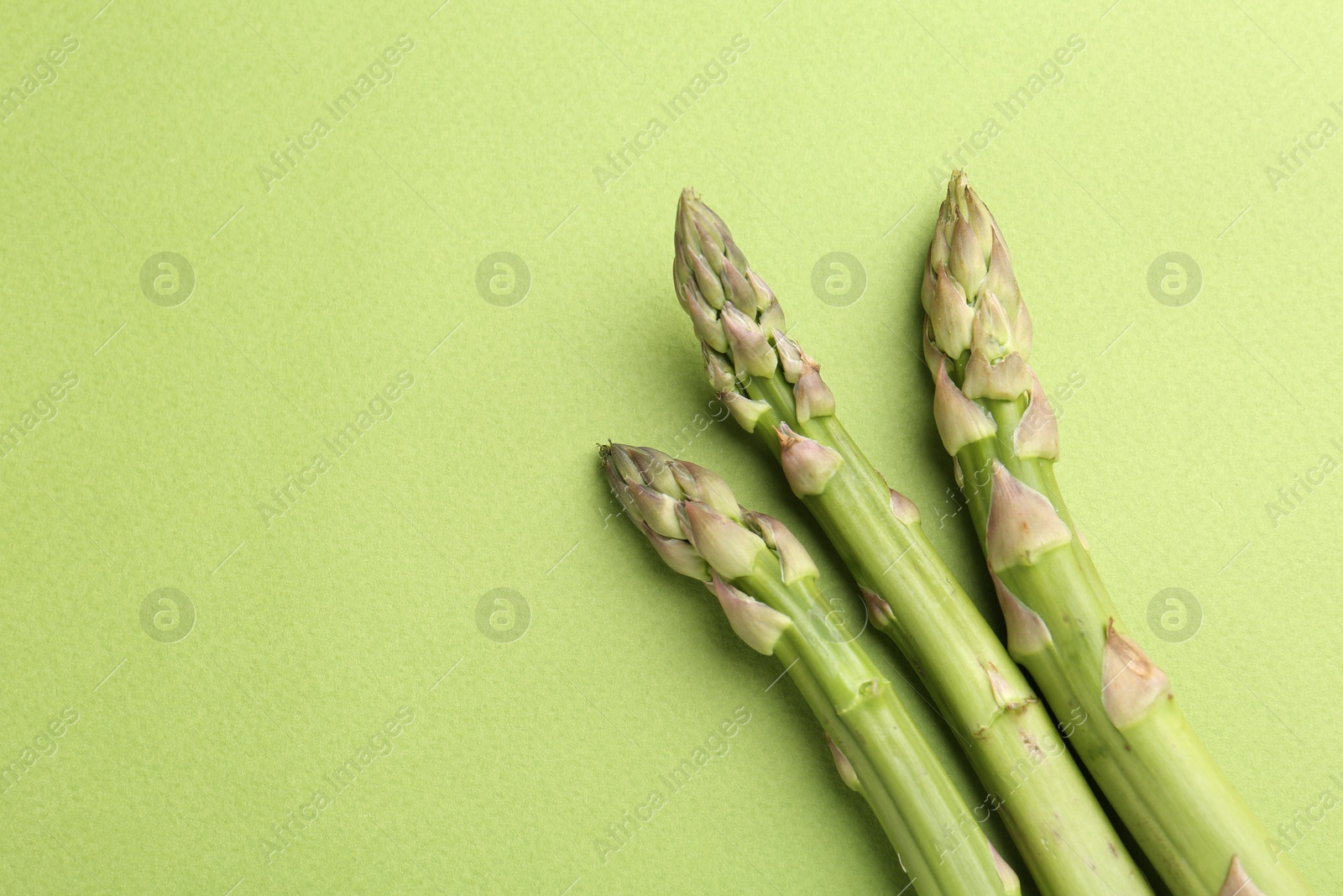 Fresh ripe raw asparagus on green background, flat lay. Space for text Photo of Fresh ripe raw asparagus on green background, flat lay. Space for text