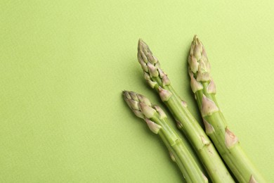 Photo of Fresh ripe raw asparagus on green background, flat lay. Space for text