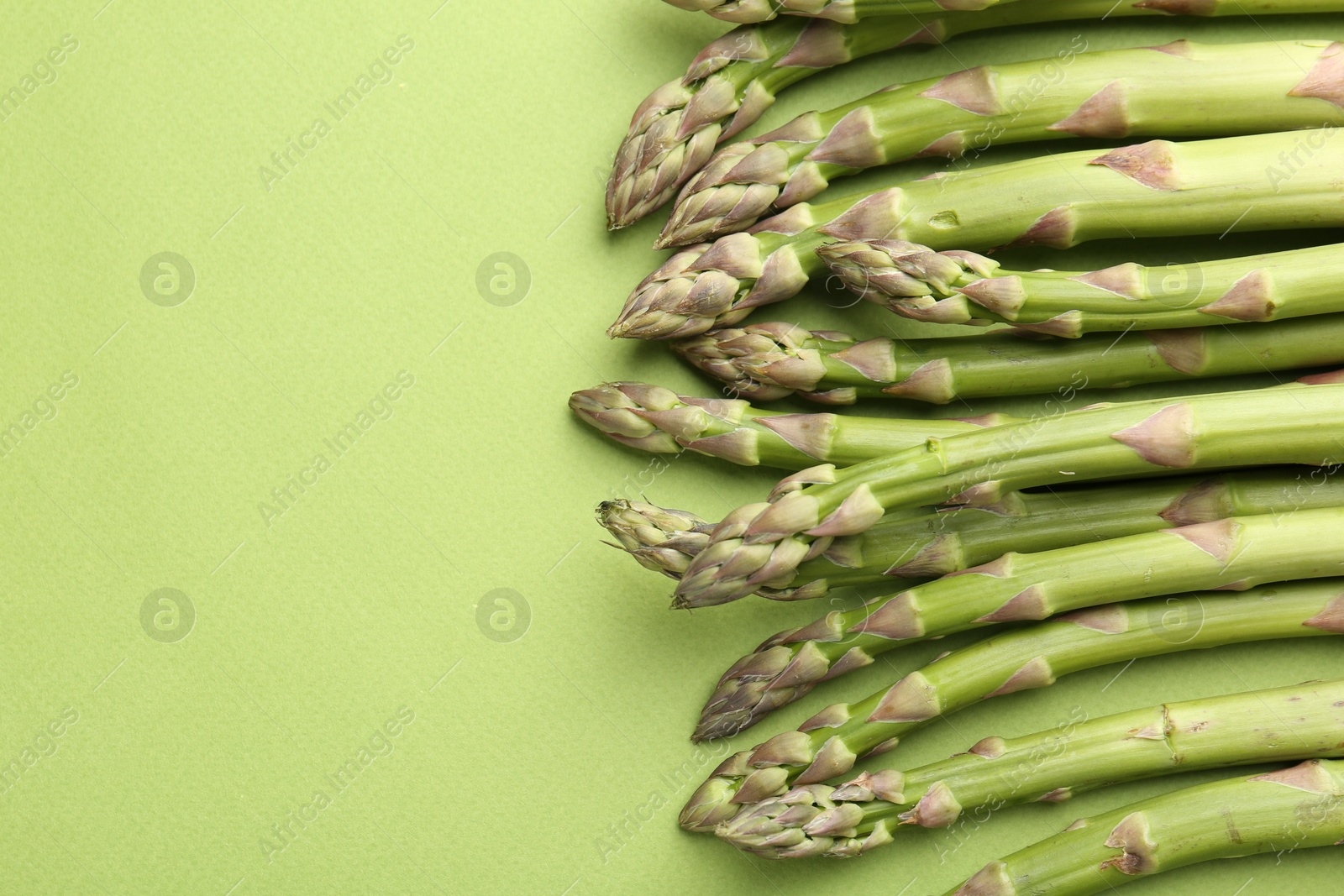 Fresh ripe raw asparagus on green background, closeup. Space for text Photo of Fresh ripe raw asparagus on green background, closeup. Space for text