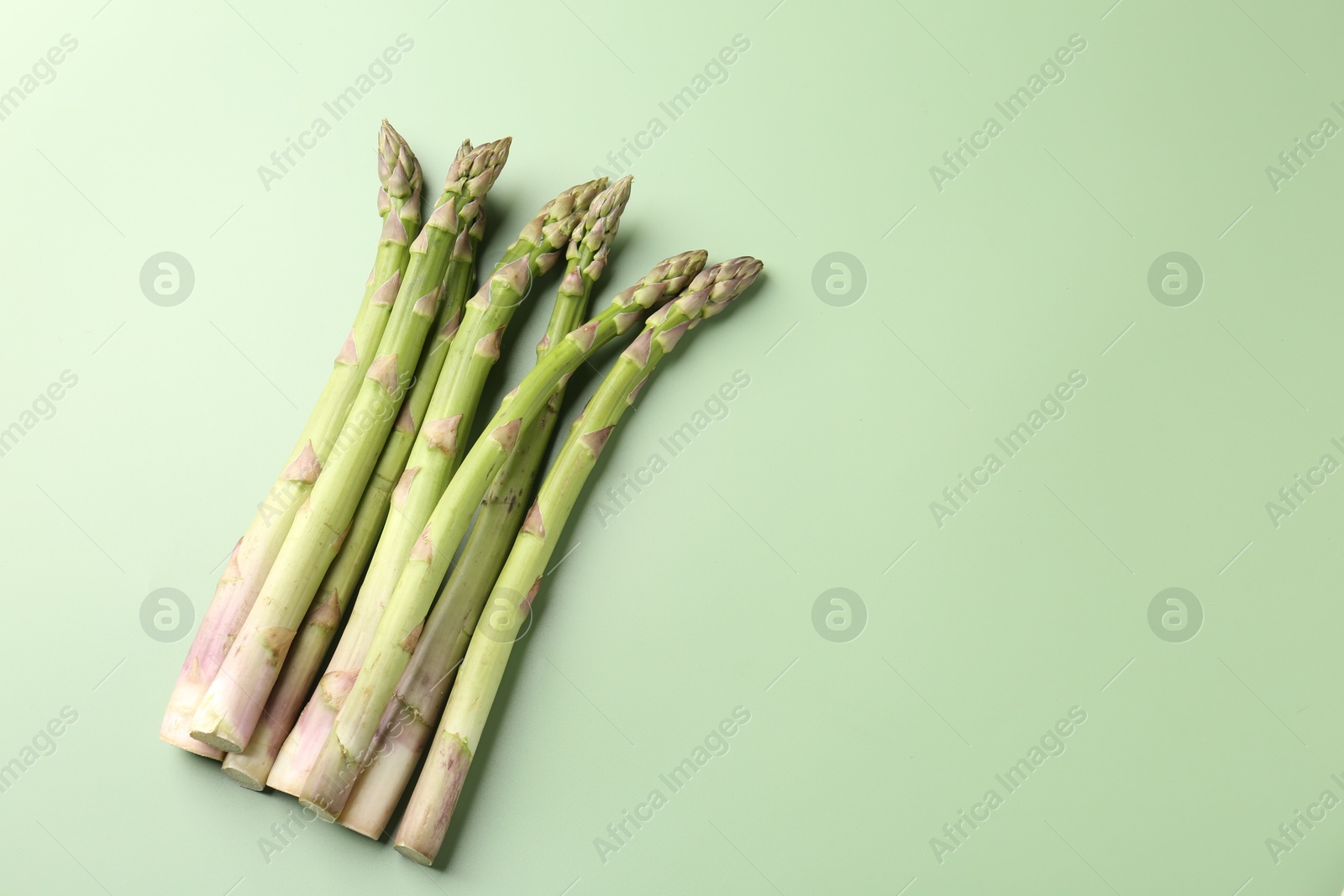 Fresh ripe raw asparagus on green background, flat lay. Space for text Photo of Fresh ripe raw asparagus on green background, flat lay. Space for text