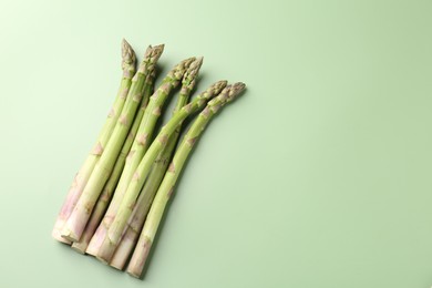 Photo of Fresh ripe raw asparagus on green background, flat lay. Space for text
