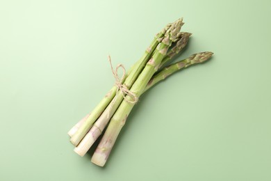 Photo of Tied raw asparagus on green background, top view