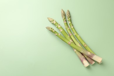 Photo of Fresh ripe raw asparagus on green background, top view. Space for text