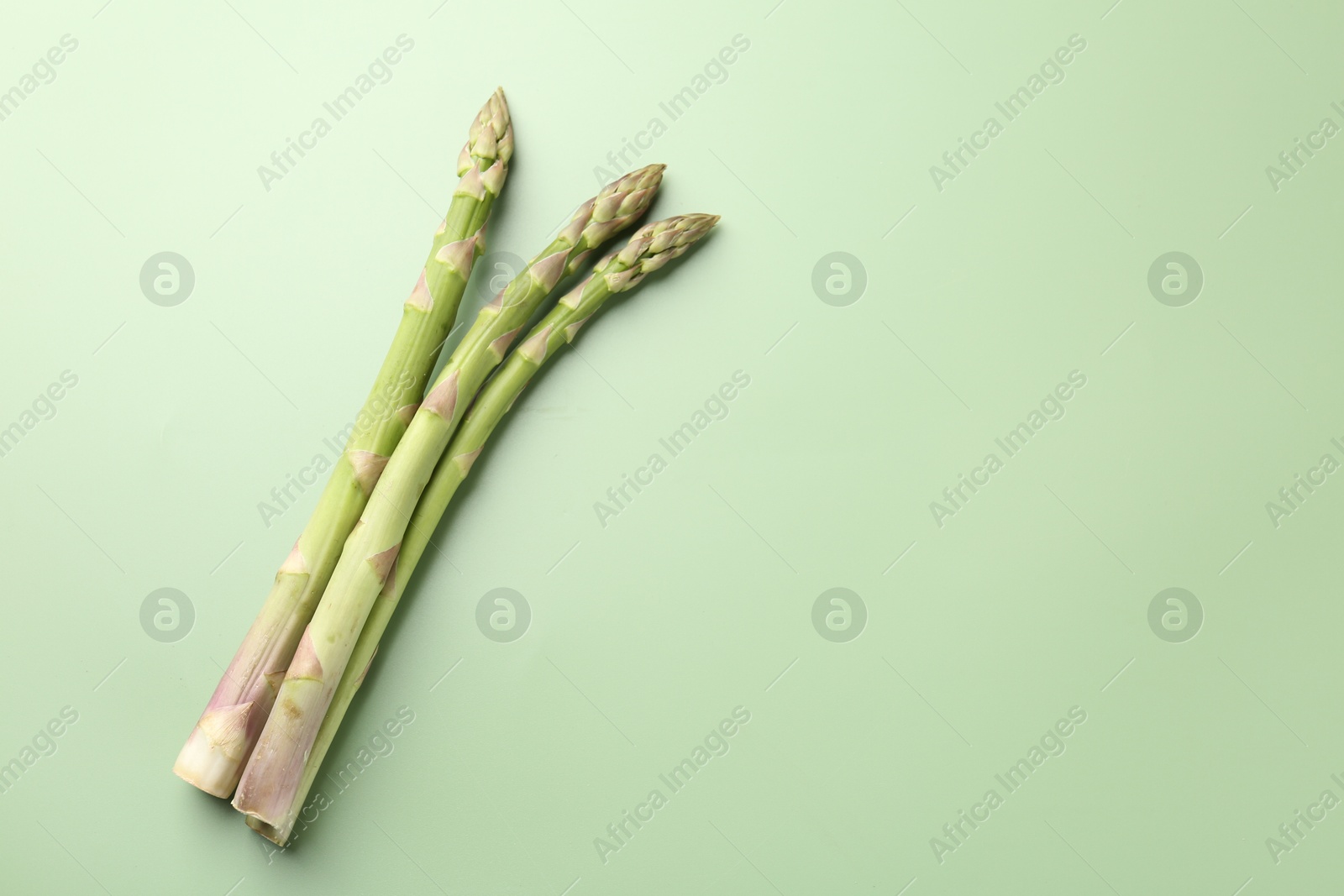 Fresh ripe raw asparagus on green background, top view. Space for text Photo of Fresh ripe raw asparagus on green background, top view. Space for text