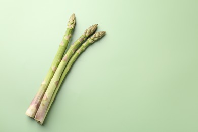 Photo of Fresh ripe raw asparagus on green background, top view. Space for text