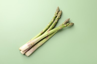 Photo of Fresh ripe raw asparagus on green background, top view