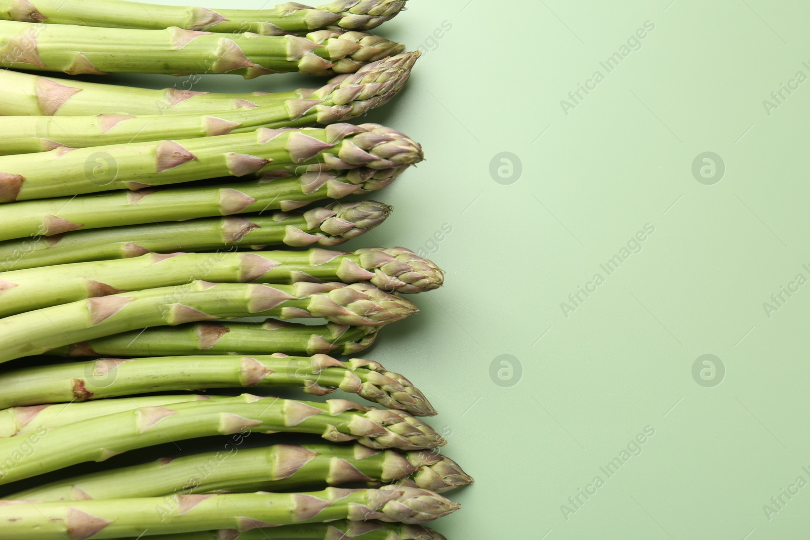 Fresh ripe raw asparagus on green background, closeup. Space for text Photo of Fresh ripe raw asparagus on green background, closeup. Space for text