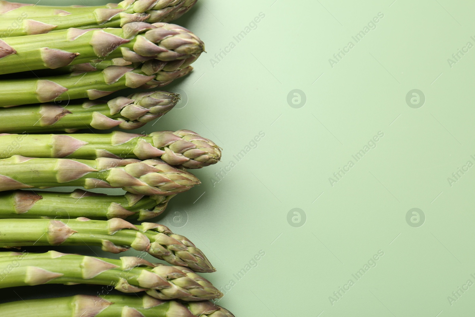 Photo of Fresh ripe raw asparagus on green background, closeup. Space for text