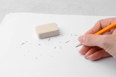 Photo of Woman with graphite pencil, eraser and paper sheet at light table, closeup
