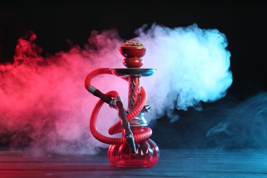 Photo of Hookah on wooden table with smoke in color lights against black background