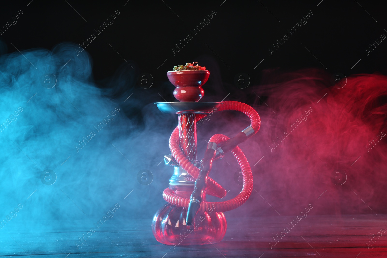 Hookah on wooden table with smoke in color lights against black background Photo of Hookah on wooden table with smoke in color lights against black background