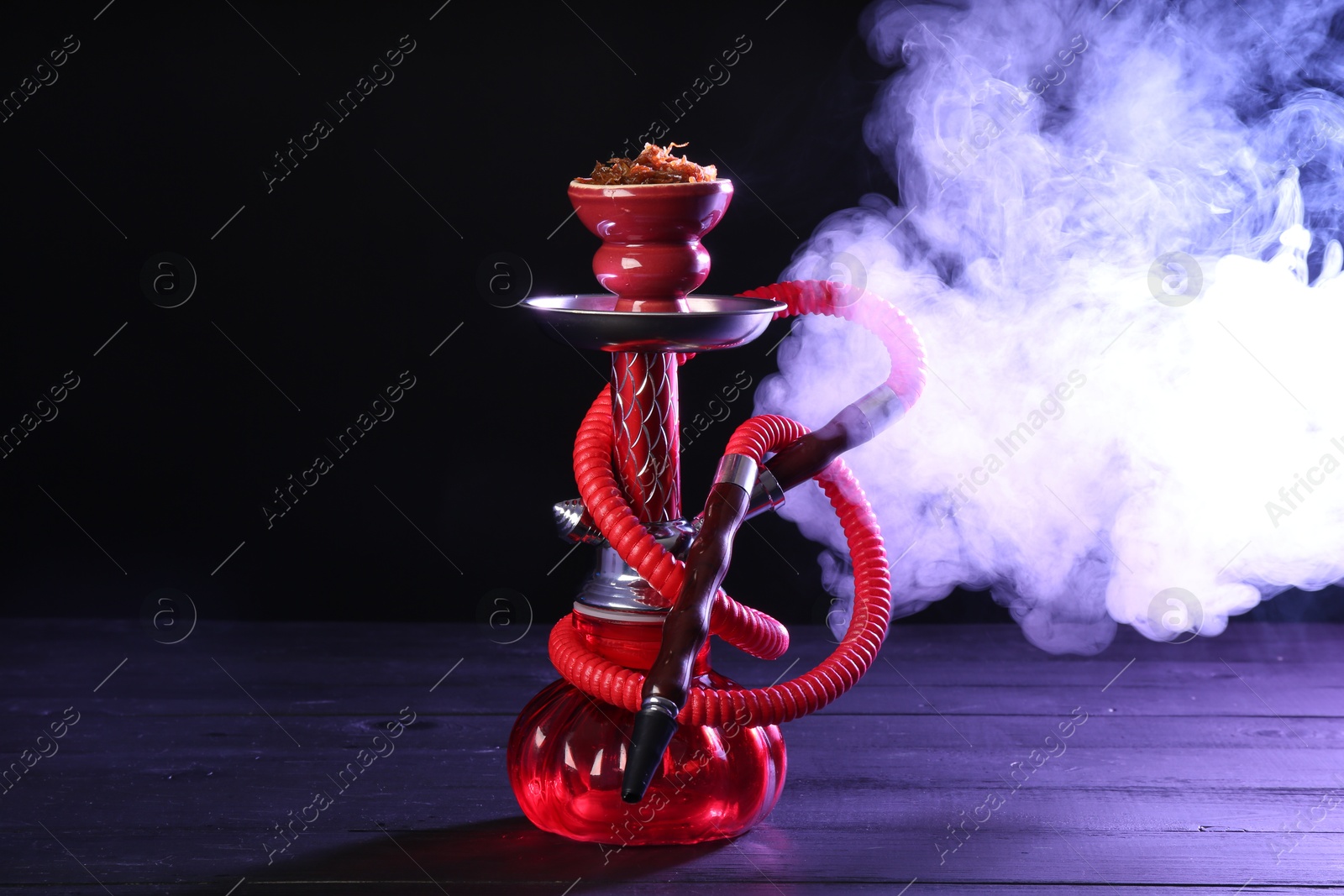 Photo of Hookah on wooden table with smoke in color lights against black background