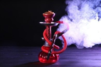 Photo of Hookah on wooden table with smoke in color lights against black background