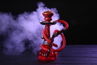 Photo of Hookah on wooden table with smoke in color lights against black background