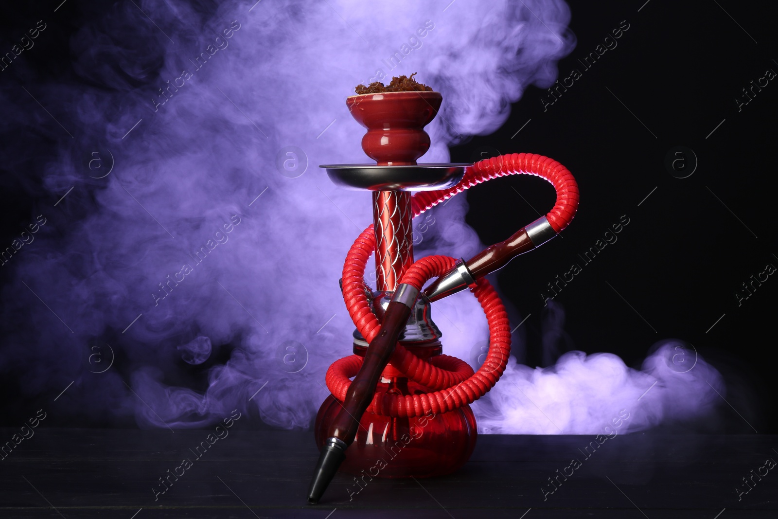 Photo of Hookah on wooden table with smoke in color lights against black background