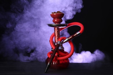 Photo of Hookah on wooden table with smoke in color lights against black background