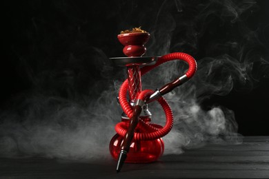 Photo of Hookah on wooden table with smoke against black background