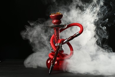 Photo of Hookah on wooden table with smoke against black background