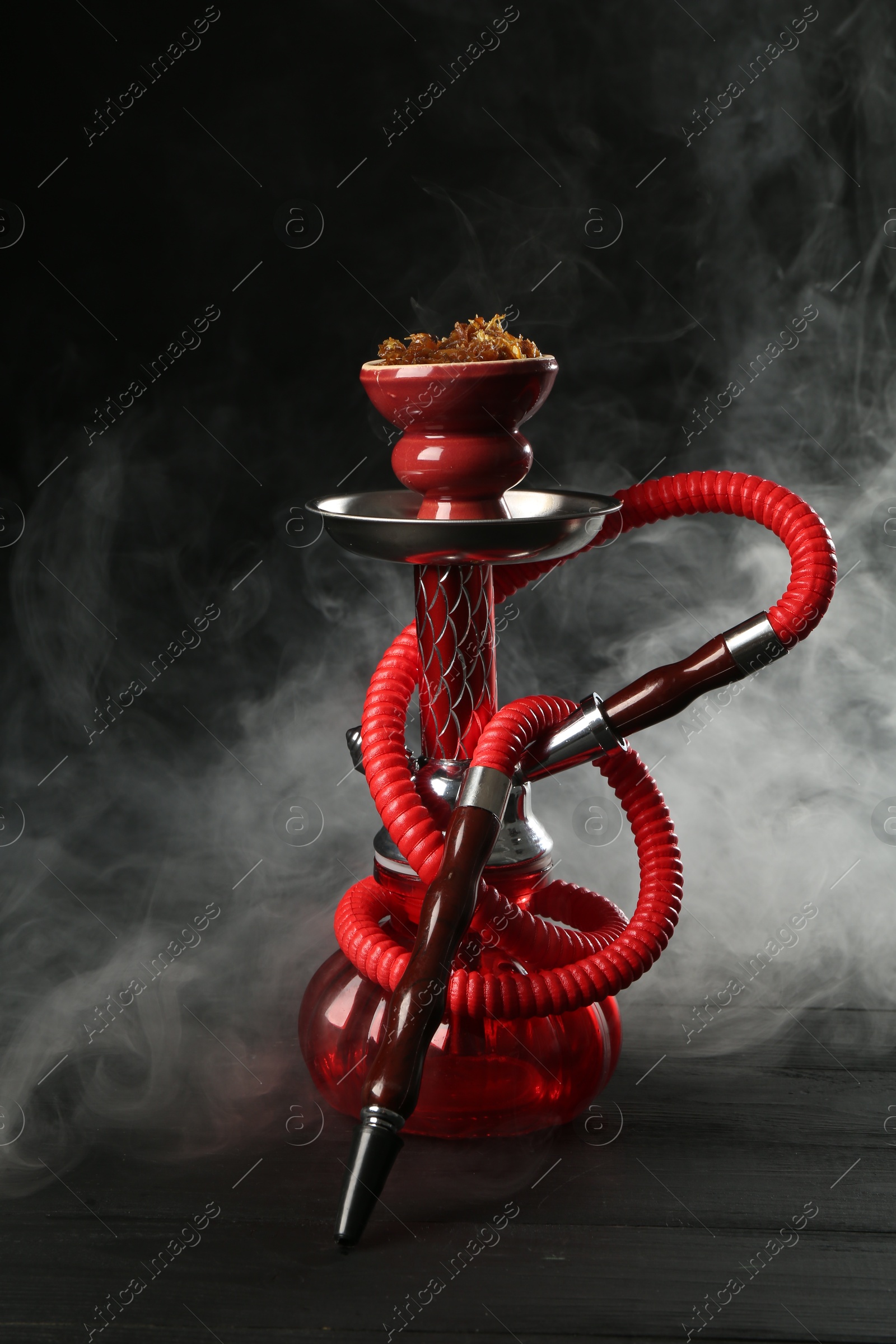 Hookah on wooden table with smoke against black background Photo of Hookah on wooden table with smoke against black background