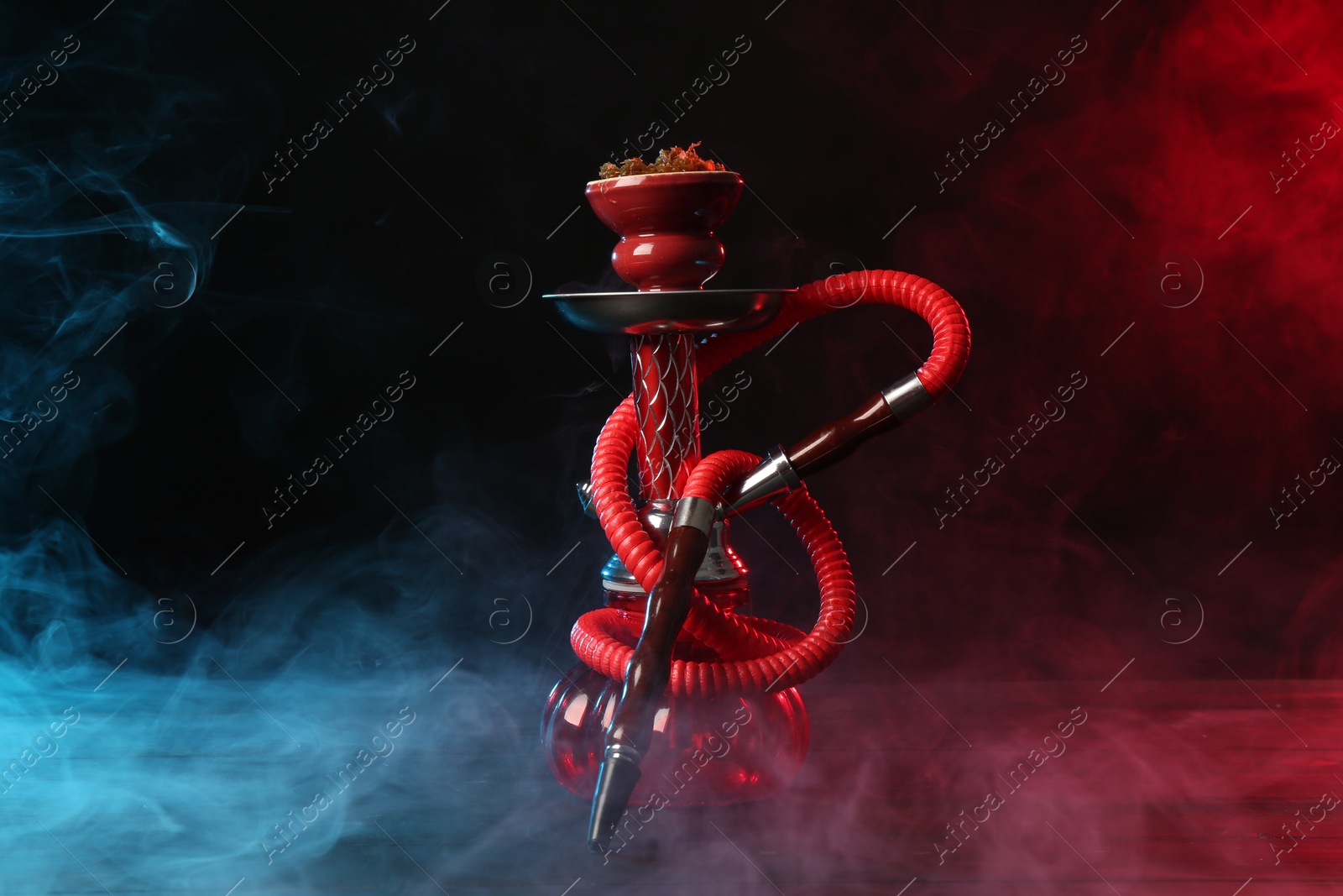 Photo of Hookah on wooden table with smoke in color lights against black background