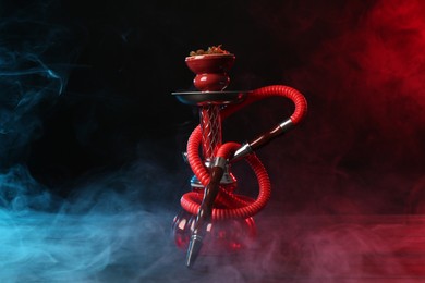 Photo of Hookah on wooden table with smoke in color lights against black background